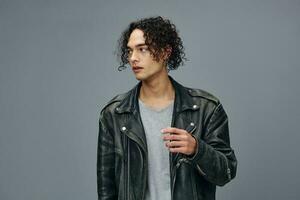 Serious adorable stylish tanned curly man leather jacket looks aside posing isolated on over gray studio background. Cool fashion offer. Huge Seasonal Sale New Collection concept. Copy space for ad photo