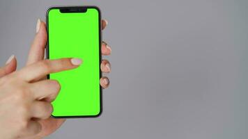 Female hands using a smartphone with a green screen on a gray background close-up. Chroma key video