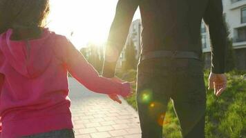 papá y hija caminar alrededor su zona a puesta de sol. niño sostiene del padre mano. lento movimiento video