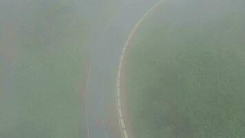 Flying through the clouds over a mountain road surrounded by green vegetation. Cars driving on the road video