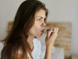 woman with a thermometer in her mouth sitting on the bed close-up photo