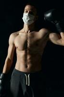 boxer in a medical mask on a black background gloves athlete naked torso photo