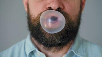 Bearded man chews chewing gum and inflates a bubble out of it. Bad habit concept video