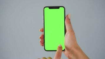 weiblich Hände mit ein Smartphone mit ein Grün Bildschirm auf ein grau Hintergrund Nahansicht. Chroma Schlüssel video