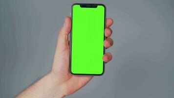 Male hands using a smartphone with a green screen on a gray background close-up. Chroma key video