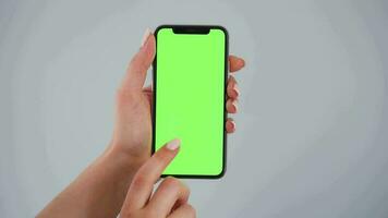 Female hands using a smartphone with a green screen on a gray background close-up. Chroma key video