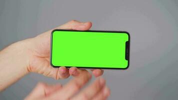 Male hands using a smartphone with a green screen on a gray background close-up. Chroma key video