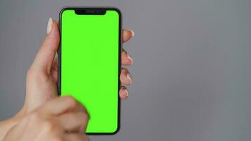 fêmea mãos usando uma Smartphone com uma verde tela em uma cinzento fundo fechar-se. croma chave video