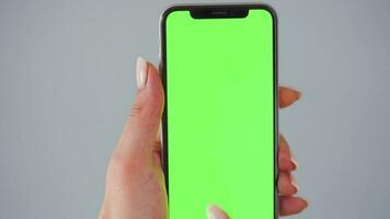 Female hands using a smartphone with a green screen on a gray background close-up. Chroma key video