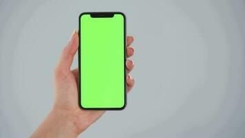 Female hands using a smartphone with a green screen on a gray background close-up. Chroma key video