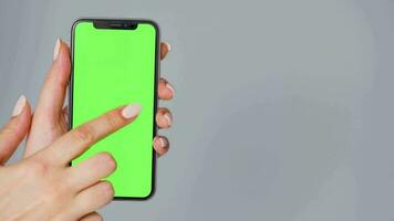 Female hands using a smartphone with a green screen on a gray background close-up. Chroma key video