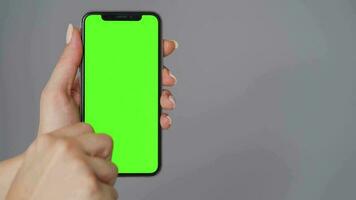 Female hands using a smartphone with a green screen on a gray background close-up. Chroma key video