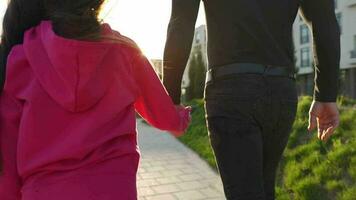Dad and daughter walk around their area at sunset. Child holds father's hand. Slow motion video