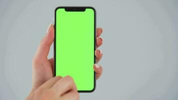 Female hands using a smartphone with a green screen on a gray background close-up. Chroma key video