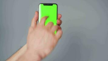 Male hands using a smartphone with a green screen on a gray background close-up. Chroma key video