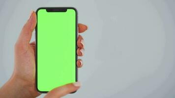 Female hands using a smartphone with a green screen on a gray background close-up. Chroma key video