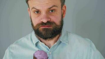 Close-up of a bearded man eating purple ice cream in a black waffle cup on a gray wall background video