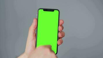 Male hands using a smartphone with a green screen on a gray background close-up. Chroma key video