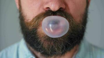 Bearded man chews chewing gum and inflates a bubble out of it. Bad habit concept video