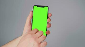 Male hands using a smartphone with a green screen on a gray background close-up. Chroma key video