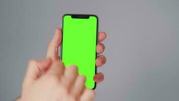 masculino manos utilizando un teléfono inteligente con un verde pantalla en un gris antecedentes de cerca. croma llave video