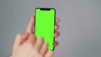 Male hands using a smartphone with a green screen on a gray background close-up. Chroma key video