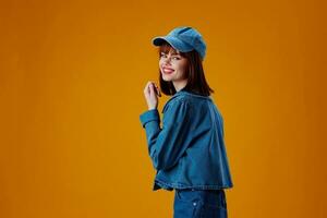 Pretty young female in a cap and denim jacket posing yellow background unaltered photo