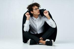 curly-haired guy straightens his jacket over his shoulders and sits on the floor in sneakers and in a suit photo