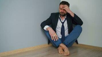 Desperate bearded man in untidy formal clothes is sitting in an empty apartment. The effects of the Covid-19 virus on the economy are unemployment, poverty, and disease. video