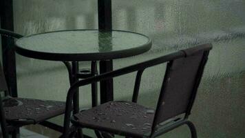 pesado chuva derrama baixa a mobília em a sacada ou terraço. gotas corre baixa a vidro do a cerca video
