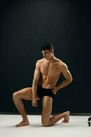 athletic man with a pumped-up body is kneeling in dark Studio panties photo