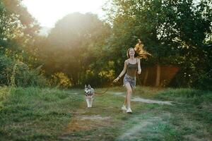 Woman and her husky dog happily running through the grass in nature in the park smile with teeth fall walk with pet, traveling with a dog friend photo