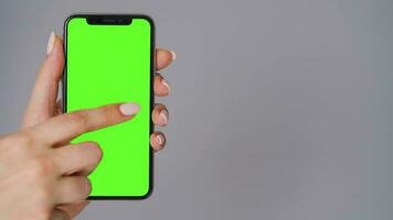 Female hands using a smartphone with a green screen on a gray background close-up. Chroma key video