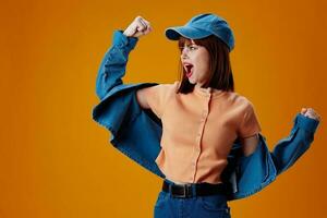 Portrait of a charming lady in a cap and denim jacket posing yellow background unaltered photo