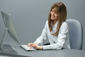 Happy pretty blonde businesswoman worker freelancer using desktop computer chatting with clients in gray modern office of support service. Remote Job, Technology Career Profession Concept. Copy space photo