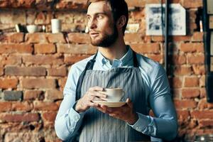 masculino camarero delantal café taza ladrillo pared restaurante Servicio foto