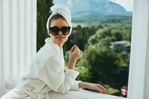 Portrait of gorgeous woman wearing sunglasses posing in a bathrobe on a balcony rest unaltered photo