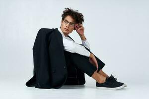 trendy guy with curly hair in a classic suit and sneakers on the floor indoors photography studio photo