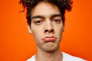 cute guy in white t-shirt curly hair grimace orange background photo