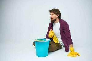 A man lies on the floor with a bucket of detergent cleaning service light background photo