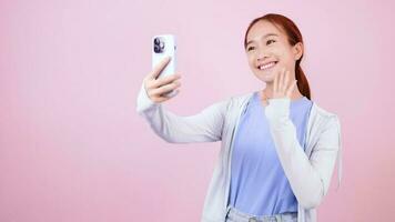 Girl in casual clothes taking selfie on video chat on smartphone with mobile app leaning against each other on pink background
