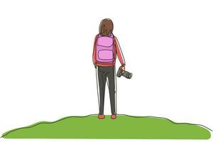 Single one line drawing back view woman holding camera standing on hill of mountain in forest landscape view with sunset. Young tourist photographer. Continuous line draw design vector illustration