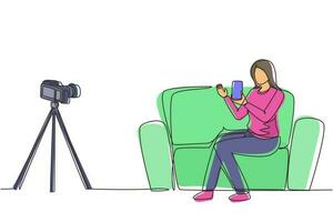 Single one line drawing female influencer filming video review smartphone on dslr camera at home. Blogger advertising tech product, streaming live. Continuous line draw design vector illustration