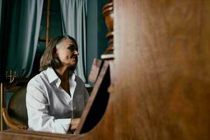 a woman in a white shirt sits on a chair next to a piano learning music photo