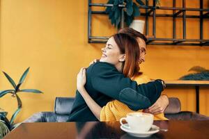 joven personas en amor abrazando mientras sentado a un mesa en un café y naranja pared interior foto