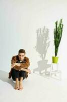Handsome guy in a brown jacket and a flower in a pot, a light room with a falling shadow photo