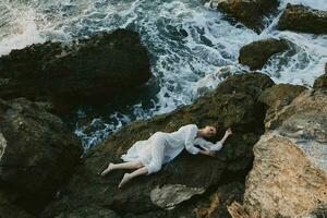 Beautiful bride in long white dress wet hair lying on a rocky cliff Summer vacation concept photo