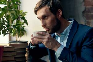 a man in a suit drinks coffee near the window of a cafe. photo