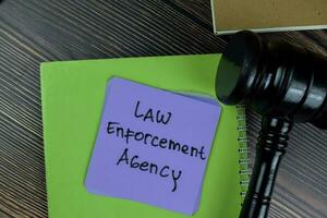 Concept of Law Enforcement Agency write on sticky notes with gavel isolated on Wooden Table. photo