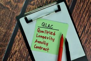 QLAC - Qualified Longevity Annuity Contract write on sticky notes isolated on Wooden Table. photo